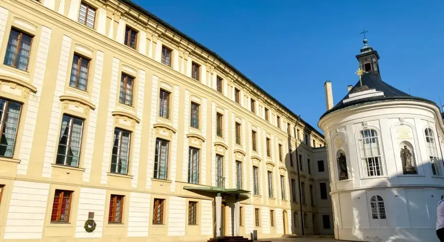 Zamek na Hradczanach, z jego żółtą fasadą i białą, okrągłą kaplicą, prezentuje się majestatycznie pod błękitnym niebem.