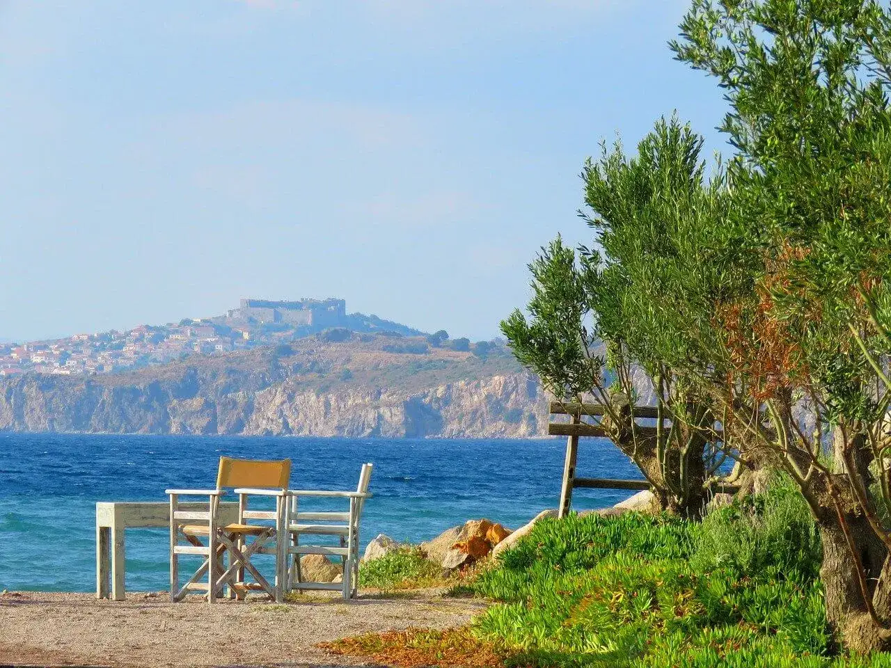 Piękna pogoda na Lesbos. Stół i krzesła czekają na plaży, w tle widać zamek i miasteczko.