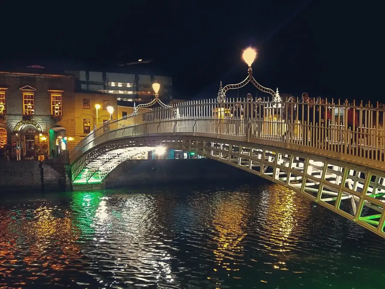 Piękny most Ha'penny w Dublinie, stolicy Irlandii, nocą. Światła odbijają się w rzece Liffey.
