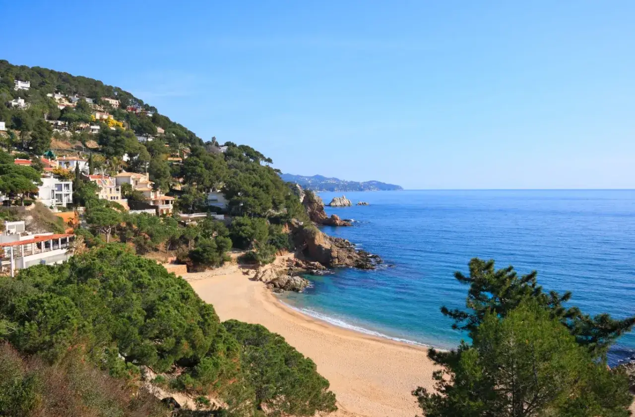 Piękna pogoda na Costa Brava: złota plaża, turkusowe morze i zielone wzgórza z białymi domkami. Idealne miejsce na wakacje.