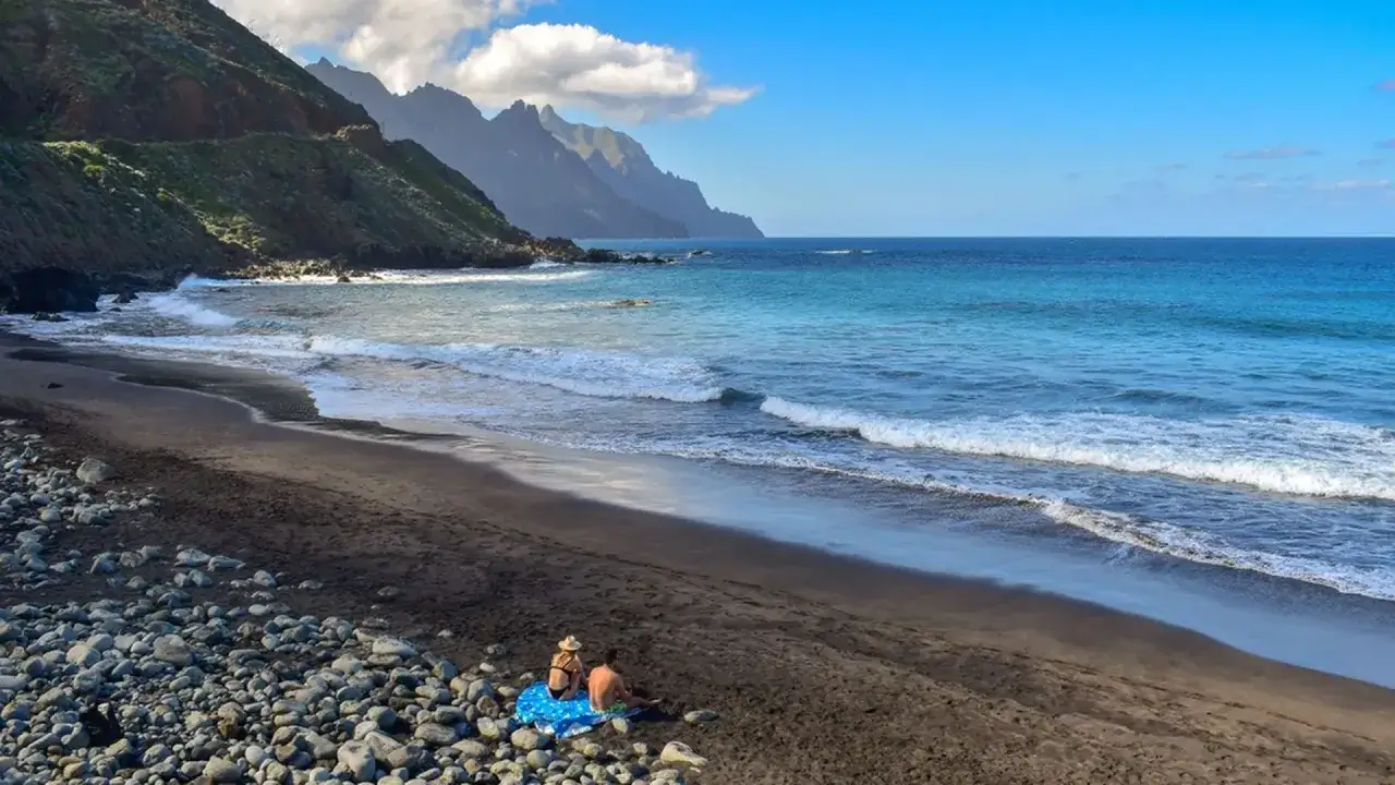 Paraiso na Teneryfie: para zrelaksowana na czarnej plaży, fale oceanu i skaliste g&oacute;ry. To jedno z najpiękniejszych miejsc na wyspie.
