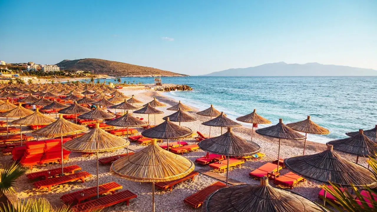 Albania pogoda październik: pusta plaża z leżakami i parasolami, morze i g&oacute;ry w tle. Idealne miejsce na spokojny wypoczynek.