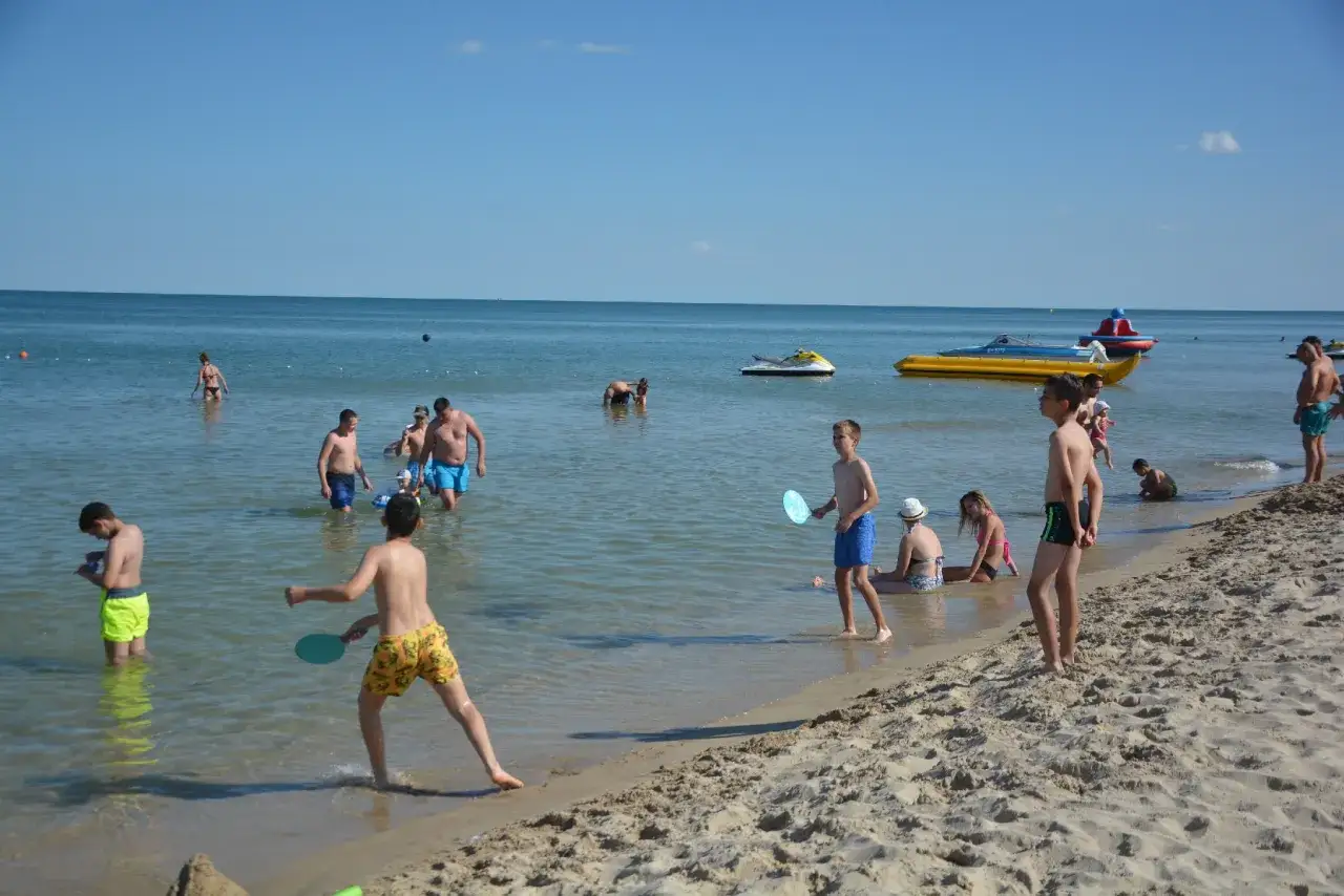 Dzieci grają w plażową piłkę wodną na słonecznej plaży w Albena Bułgaria. W tle widać łodzie i skutery wodne.