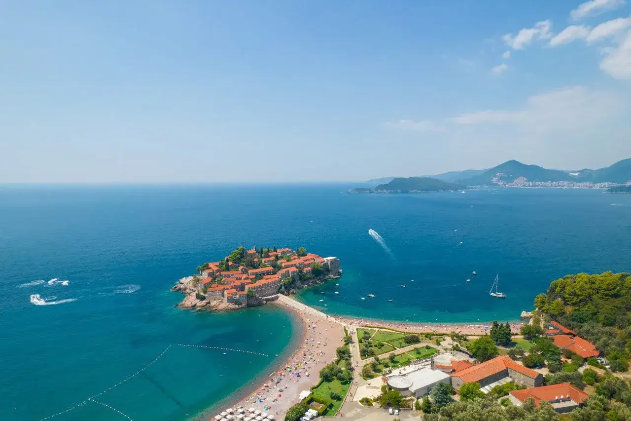 Idealna czarnog&oacute;ra pogoda wrzesień: wyspa Sveti Stefan, plaża, błękitne morze i g&oacute;ry w tle.