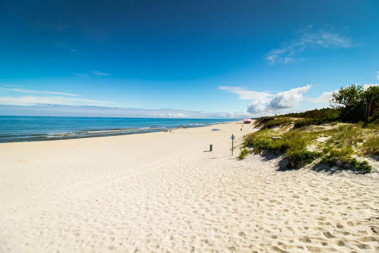 Piękna, piaszczysta plaża na Mierzei Wiślanej. W oddali widać morze i kilka os&oacute;b. To idealne miejsce na relaks i podziwianie widok&oacute;w.