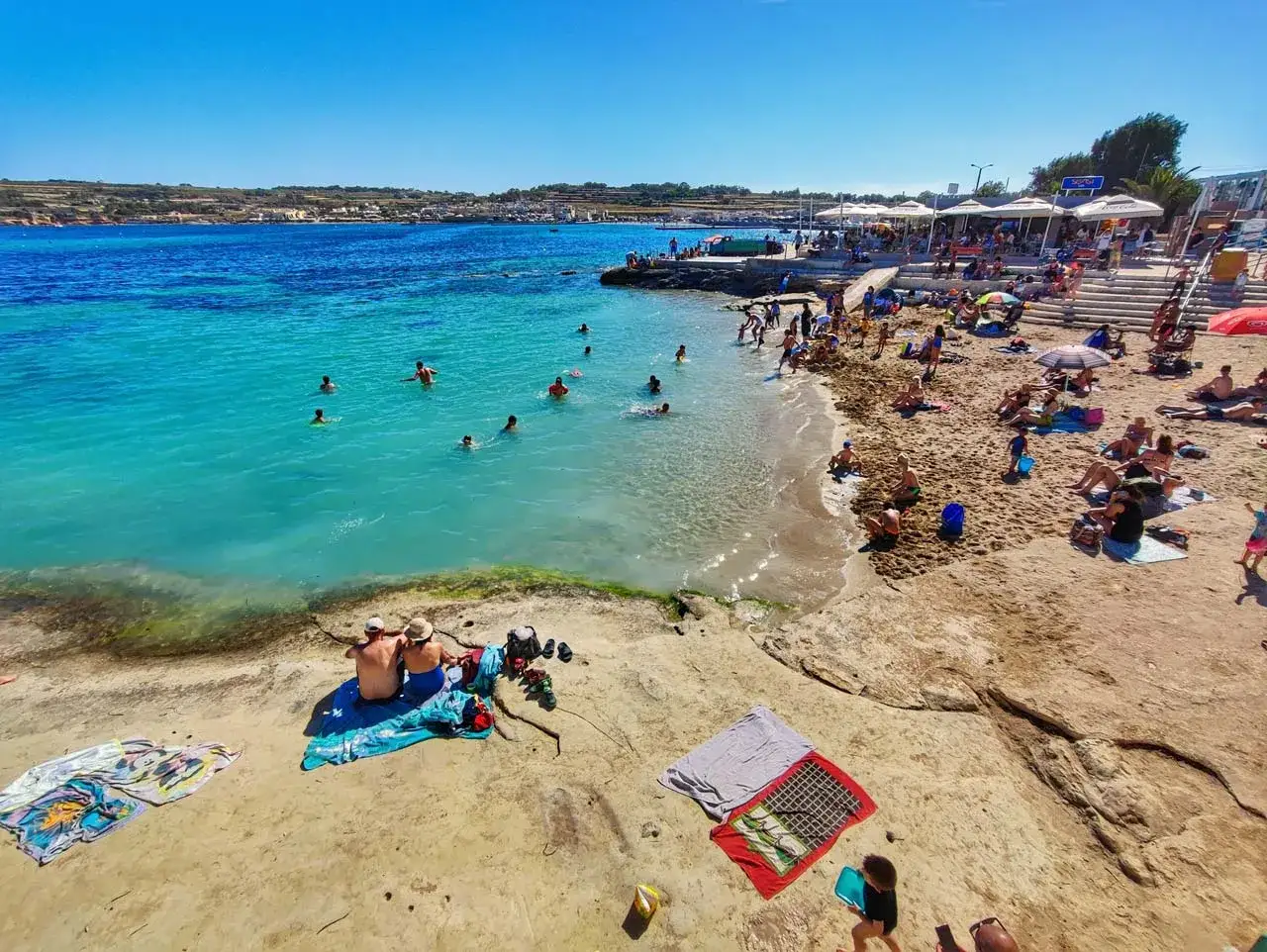 Malta pogoda w styczniu: ludzie kąpią się w turkusowym morzu i opalają na piaszczystej plaży.