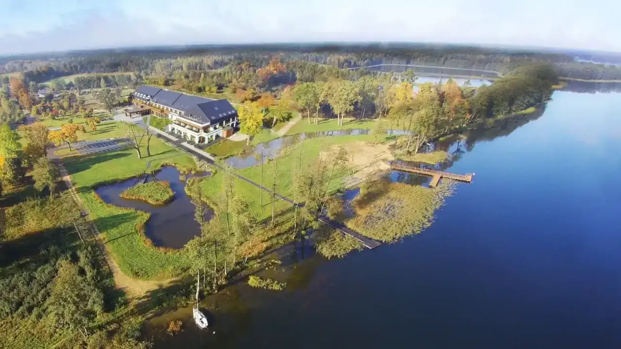 Hotel nad jeziorem, otoczony jesiennym lasem, z pomostem i ł&oacute;dką. Idealne mazury atrakcje dla miłośnik&oacute;w spokoju i natury.